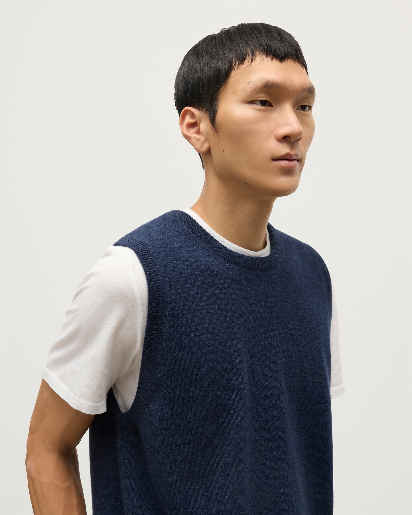 MODEL WEARS JOHNSTONS OF ELGIN MENS LENNOX SLEEVELESS CREW NAVY 100% CASHMERE, OVER A WHITE SHORT SLEEVE T-SHIRT WITH WHITE JEANS KAP05243HD7350