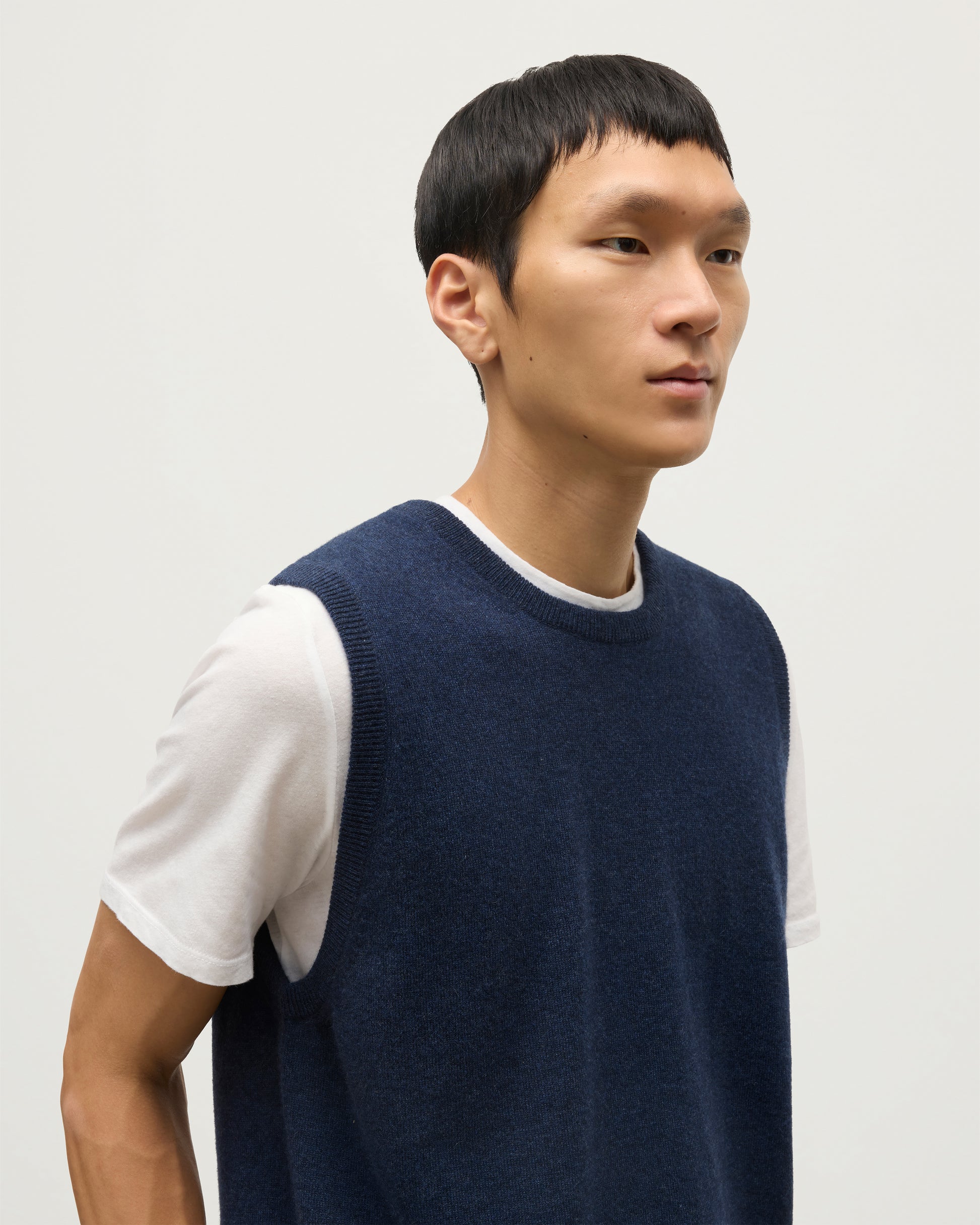 MODEL WEARS JOHNSTONS OF ELGIN MENS LENNOX SLEEVELESS CREW NAVY 100% CASHMERE, OVER A WHITE SHORT SLEEVE T-SHIRT WITH WHITE JEANS KAP05243HD7350