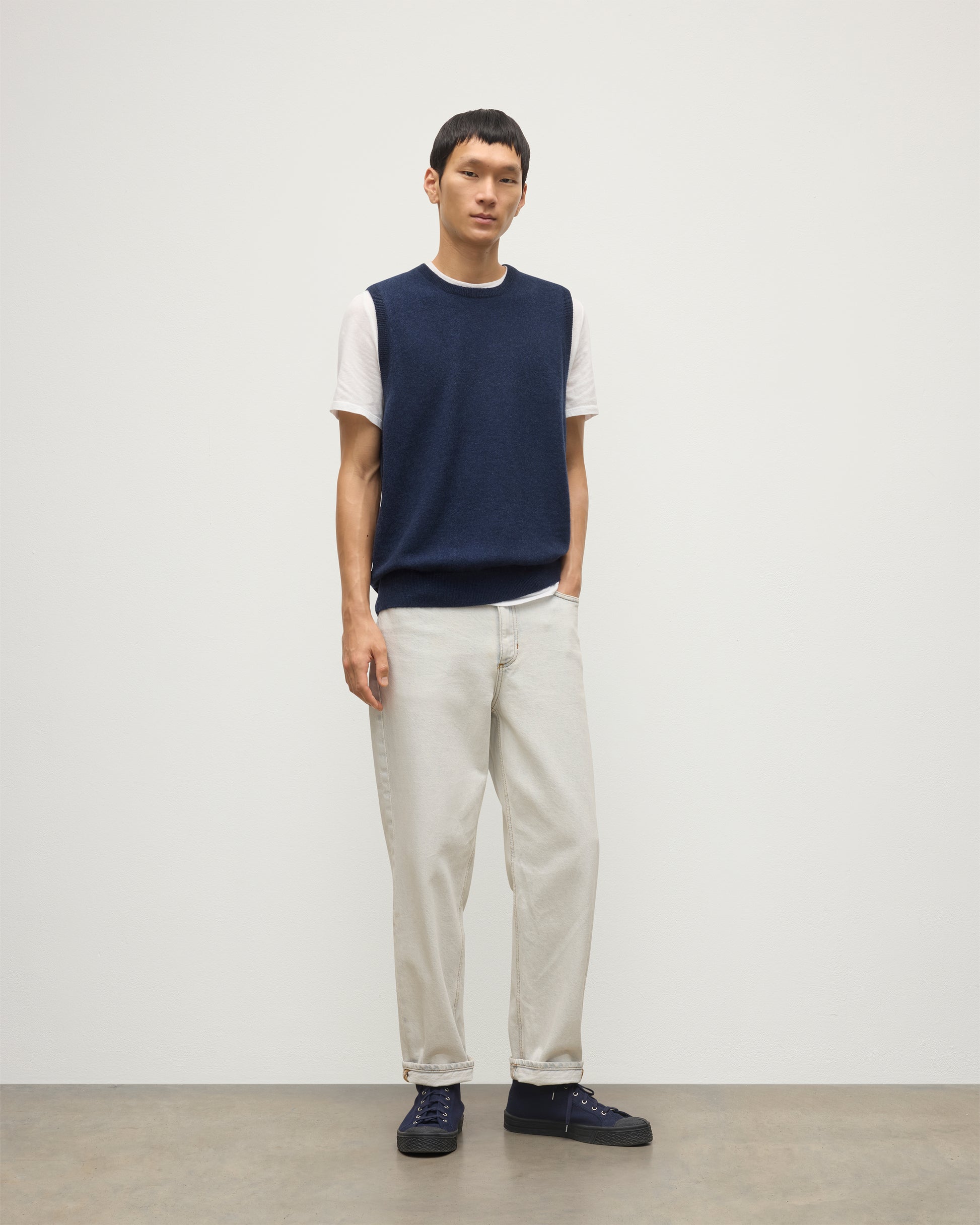 MODEL WEARS JOHNSTONS OF ELGIN MENS LENNOX SLEEVELESS CREW NAVY 100% CASHMERE, OVER A WHITE SHORT SLEEVE T-SHIRT WITH WHITE JEANS KAP05243HD7350