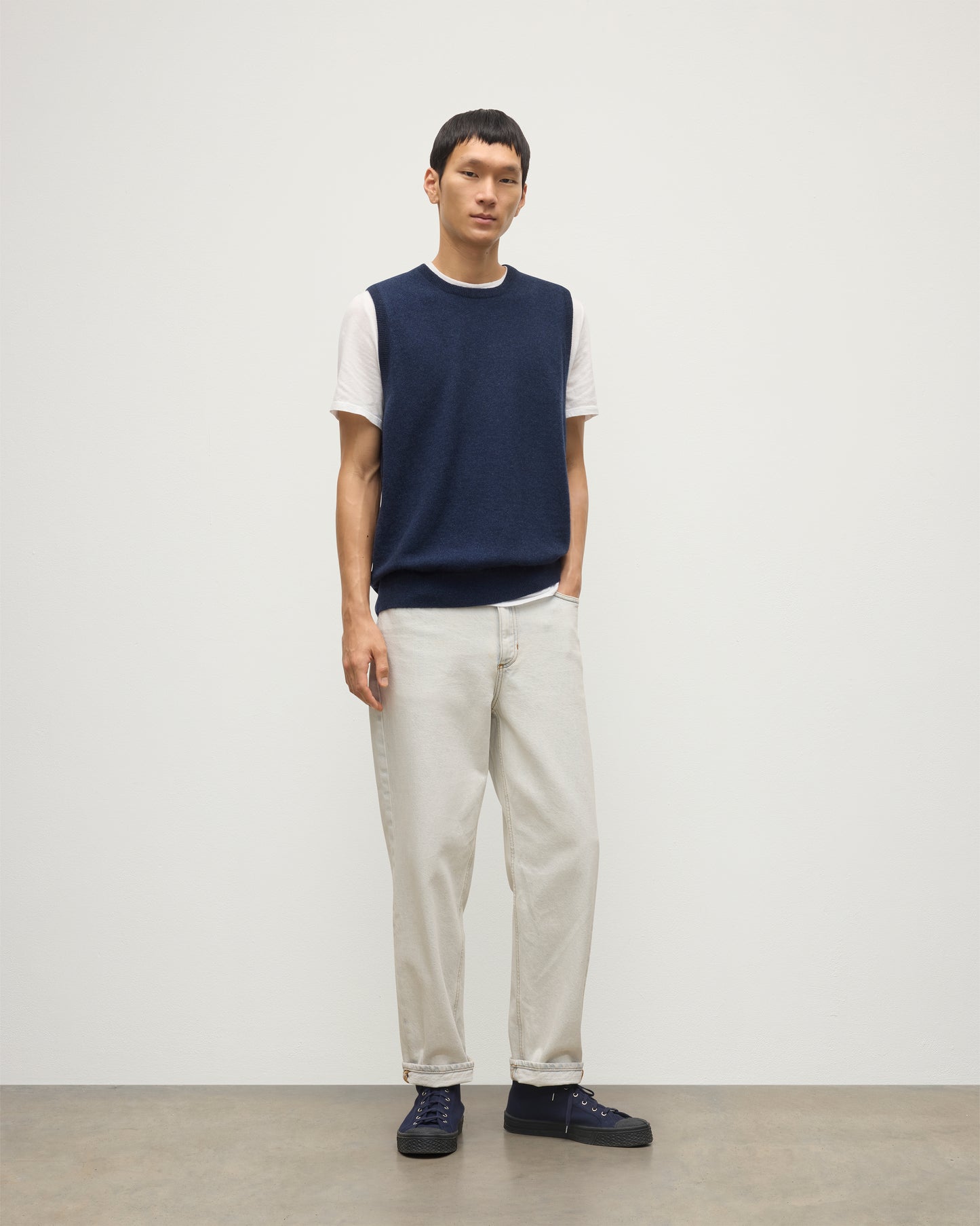 MODEL WEARS JOHNSTONS OF ELGIN MENS LENNOX SLEEVELESS CREW NAVY 100% CASHMERE, OVER A WHITE SHORT SLEEVE T-SHIRT WITH WHITE JEANS KAP05243HD7350