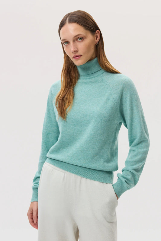 Model wears Johnstons of Elgin SS25 Women's Knitwear Jade Classic Cashmere Roll Neck Sweater with white culottes KAP05275HC4284