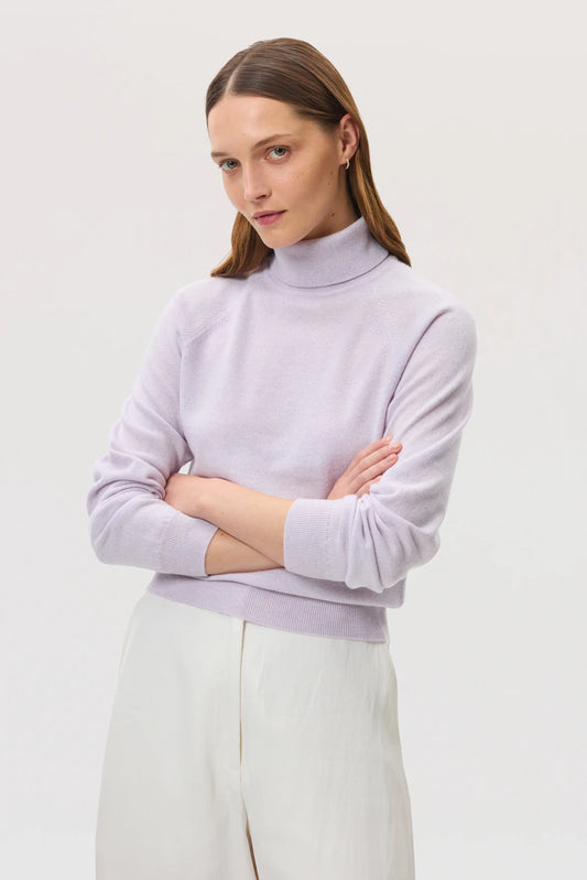 Model wears Johnstons of Elgin SS25 Women's Knitwear Lavender Classic Cashmere Roll Neck Jumper with white trousers KAP05275HD0086