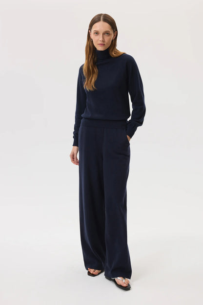 Model wears Johnstons of Elgin SS25 Women's Knitwear Navy Classic Cashmere Roll Neck Sweater with matching cashmere culottes on a white background  KAP05275SD7286