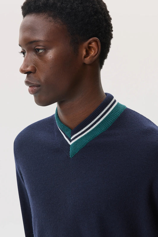 Model wears Johnstons of Elgin SS25 Men's Knitwear Navy Cashmere V Neck Sweater with Striped Trim in emerald KAP05410Q25119