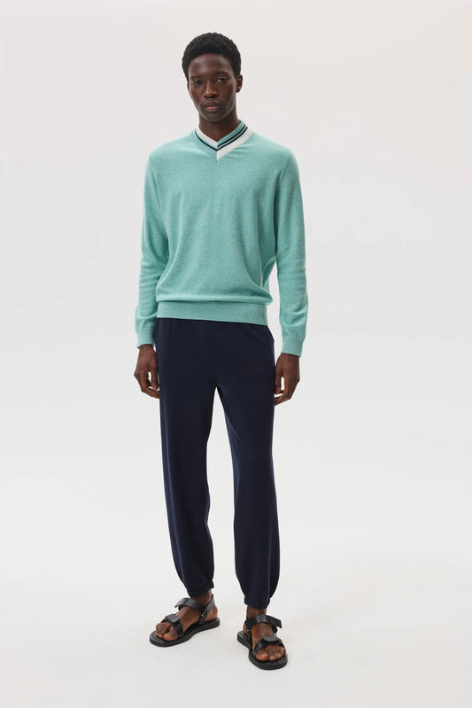 Model wears Johnstons of Elgin SS25 Men's Knitwear Jade Cashmere V Neck  Jumper with Striped Trim in navy and white, with navy cashmere joggers, on a white background KAP05410Q25122