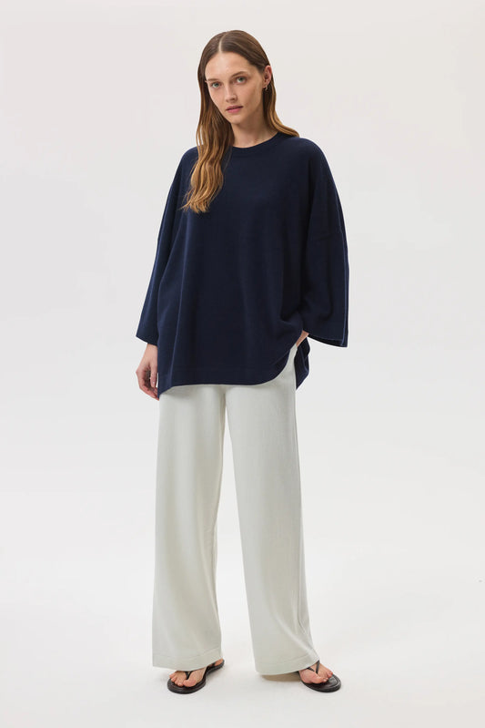 Model wears Johnstons of Elgin SS25 Women's Knitwear Navy Relaxed Featherlight Cashmere Jumper with white trousers and black sandals KAP05426SD7286