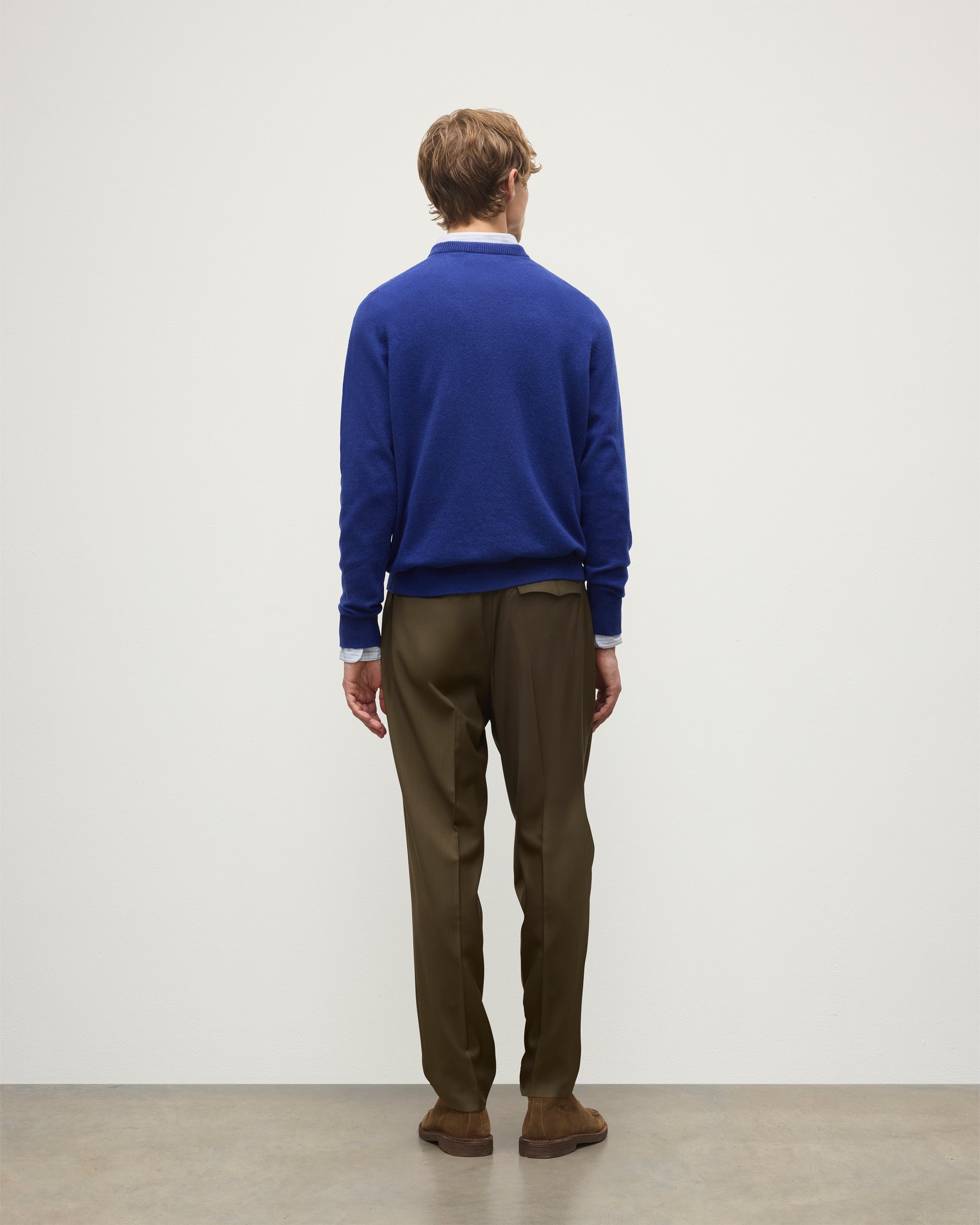 MODEL WEARS JOHNSTONS OF ELGIN MENS RORY CREW CLASSIC JUMPER BLUE 100% CASHMERE OVER A LIGHT BLUE SHIRT WITH OLIVE GREEN TROUSERS KAP05471SD5326