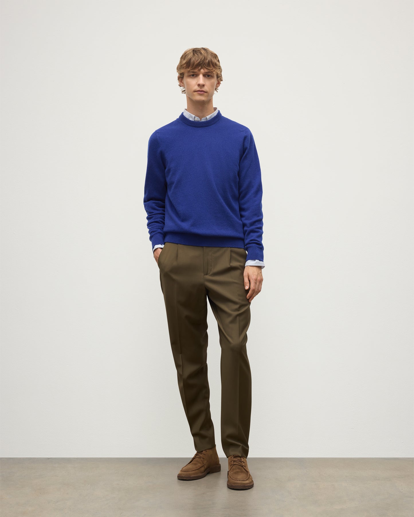 MODEL WEARS JOHNSTONS OF ELGIN MENS RORY CREW CLASSIC JUMPER BLUE 100% CASHMERE OVER A LIGHT BLUE SHIRT WITH OLIVE GREEN TROUSERS KAP05471SD5326