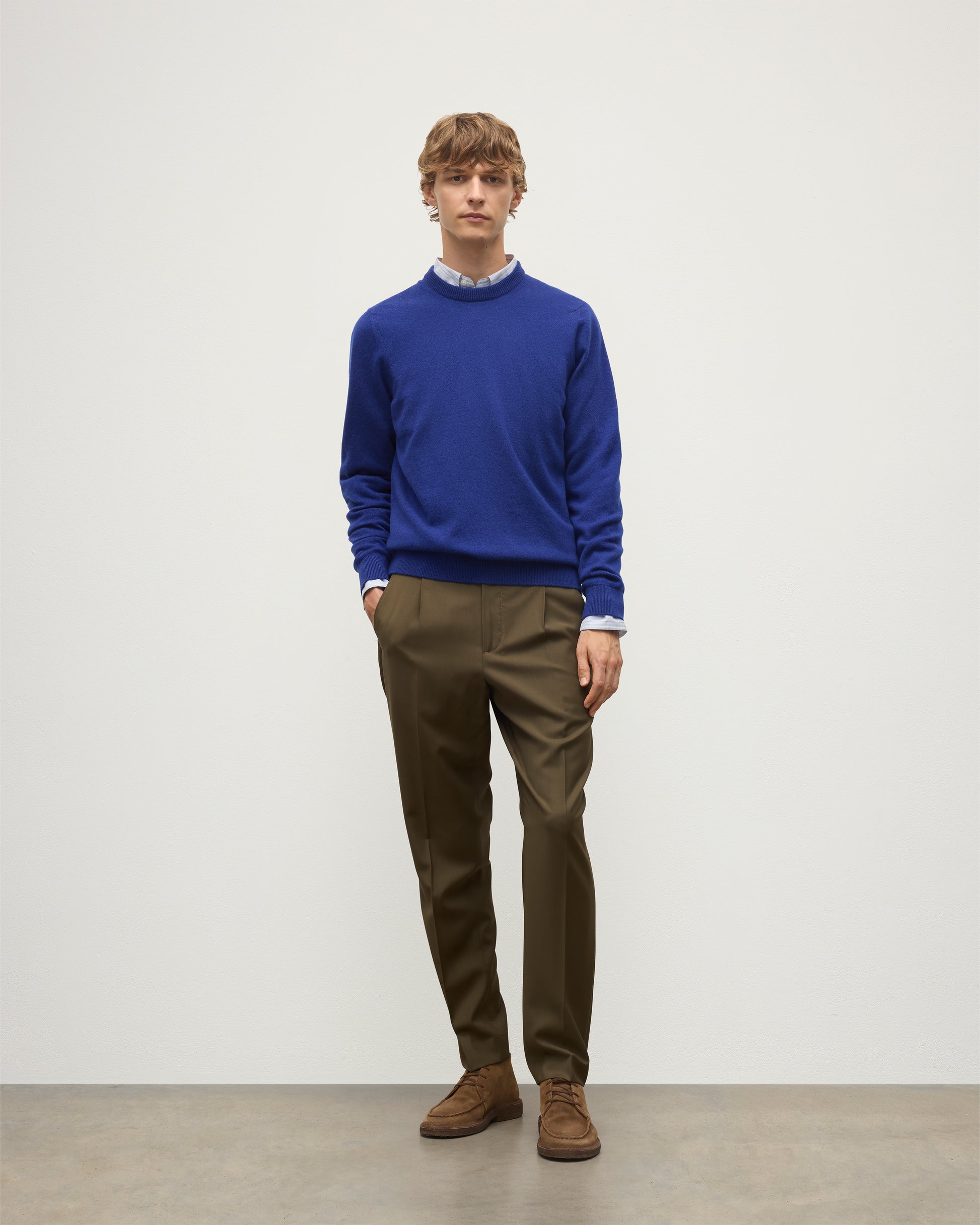 MODEL WEARS JOHNSTONS OF ELGIN MENS RORY CREW CLASSIC JUMPER BLUE 100% CASHMERE OVER A LIGHT BLUE SHIRT WITH OLIVE GREEN TROUSERS KAP05471SD5326