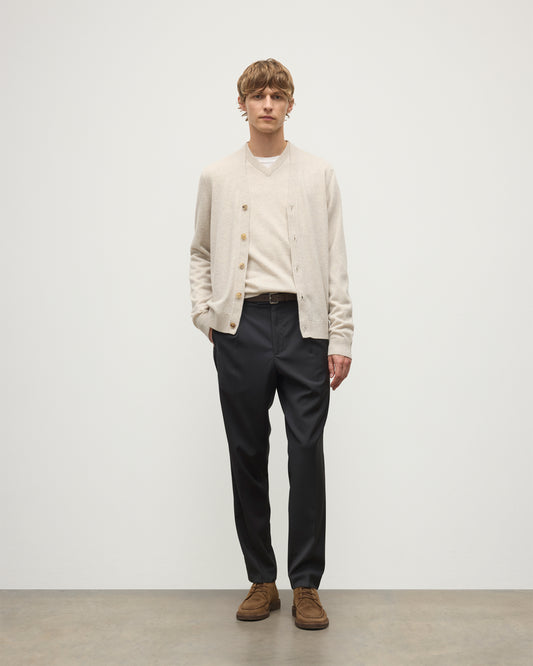 MODEL WEARS JOHNSTONS OF ELGIN MENS RORY VEE NECK CLASSIC CARDIGAN NATURAL 100% CASHMERE OVER A MATCHING V NECK SWEATER WITH GREY TROIUSERS KAP05576HA0402