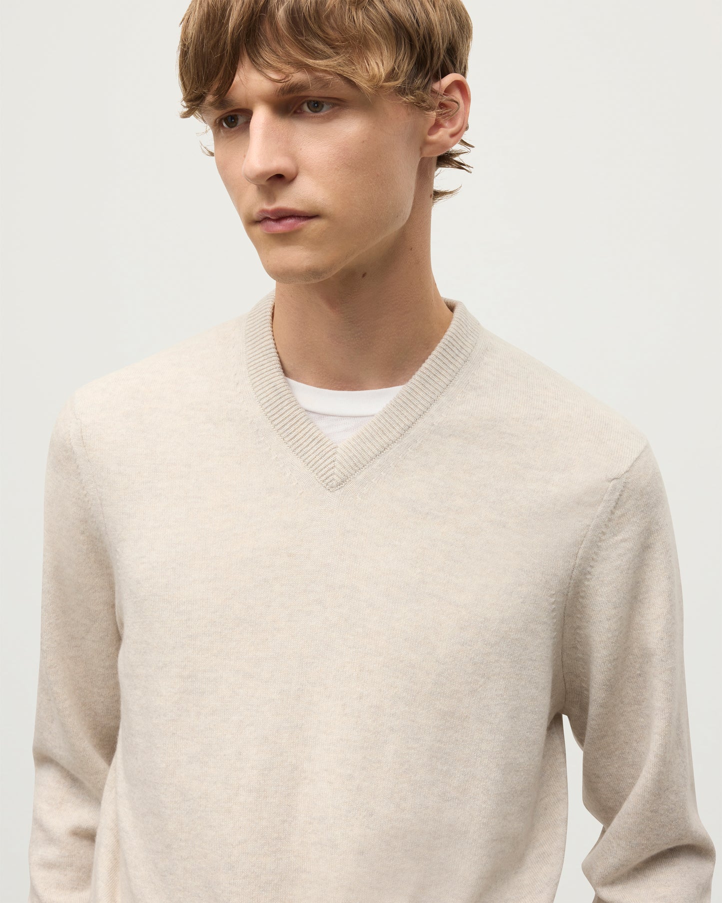MODEL WEARS JOHNSTONS OF ELGIN MENS RORY VEE NECK CLASSIC JUMPER NATURAL 100% CASHMERE, OVER A WHITE T-SHIRT WITH NAVY TROUSERS  KAP05594HA0402
