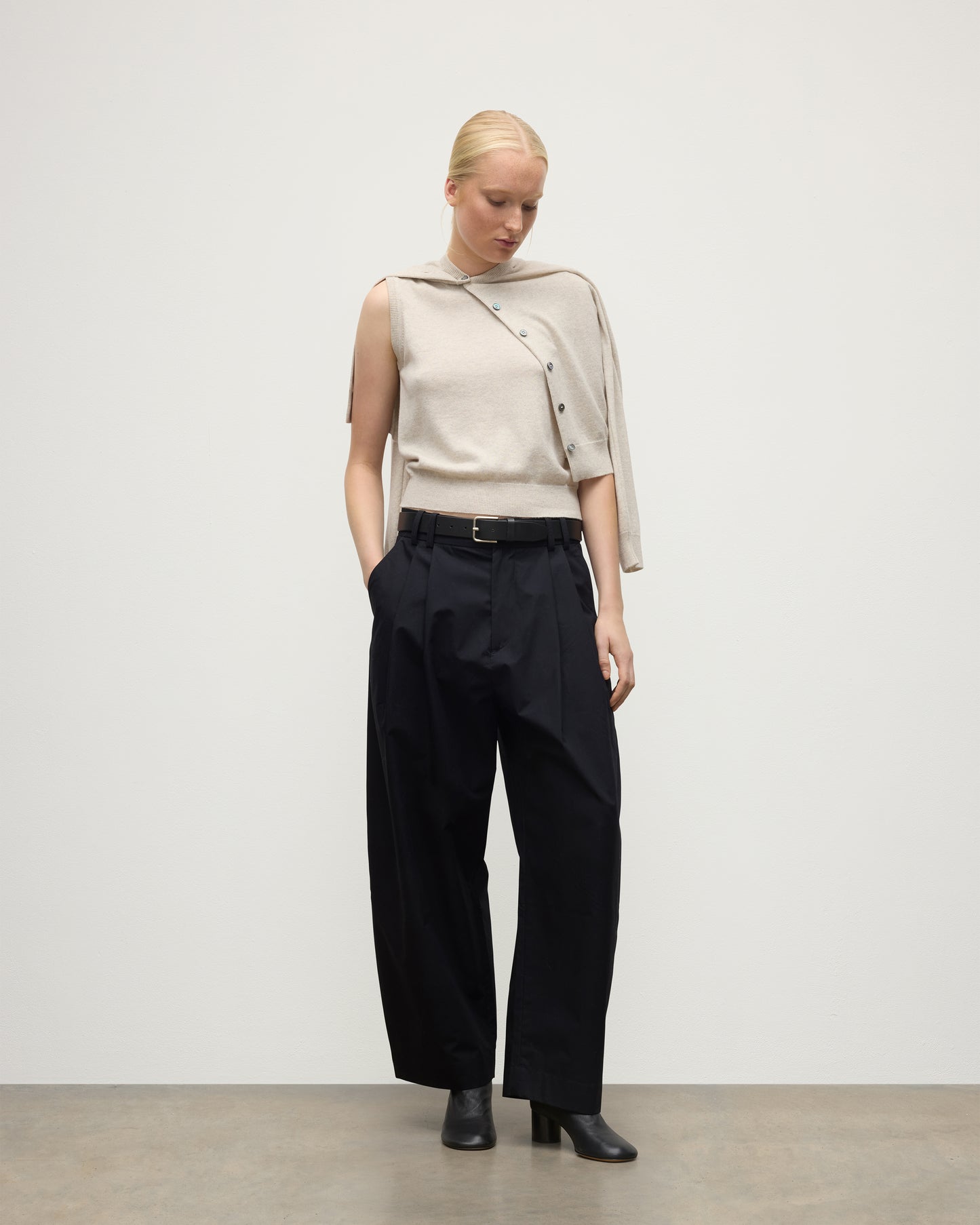 MODEL WEARS JOHNSTONS OF ELGIN WOMENS IRIS CLASSIC SLEEVELESS CREW NATURAL 100% CASHMERE WITH MATCHING CARDIGAN DRAPED OVER SHOULDERS, WITH NAVY TROUSERS AND BLACK BOOTS  KAP05705HA0402