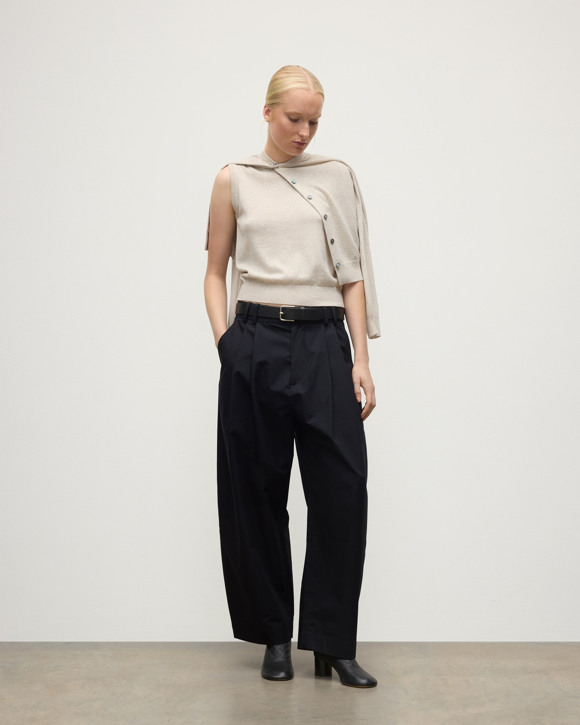 MODEL WEARS JOHNSTONS OF ELGIN WOMENS IRIS CLASSIC SLEEVELESS CREW NATURAL 100% CASHMERE WITH MATCHING CARDIGAN DRAPED OVER SHOULDERS, WITH NAVY TROUSERS AND BLACK BOOTS  KAP05705HA0402