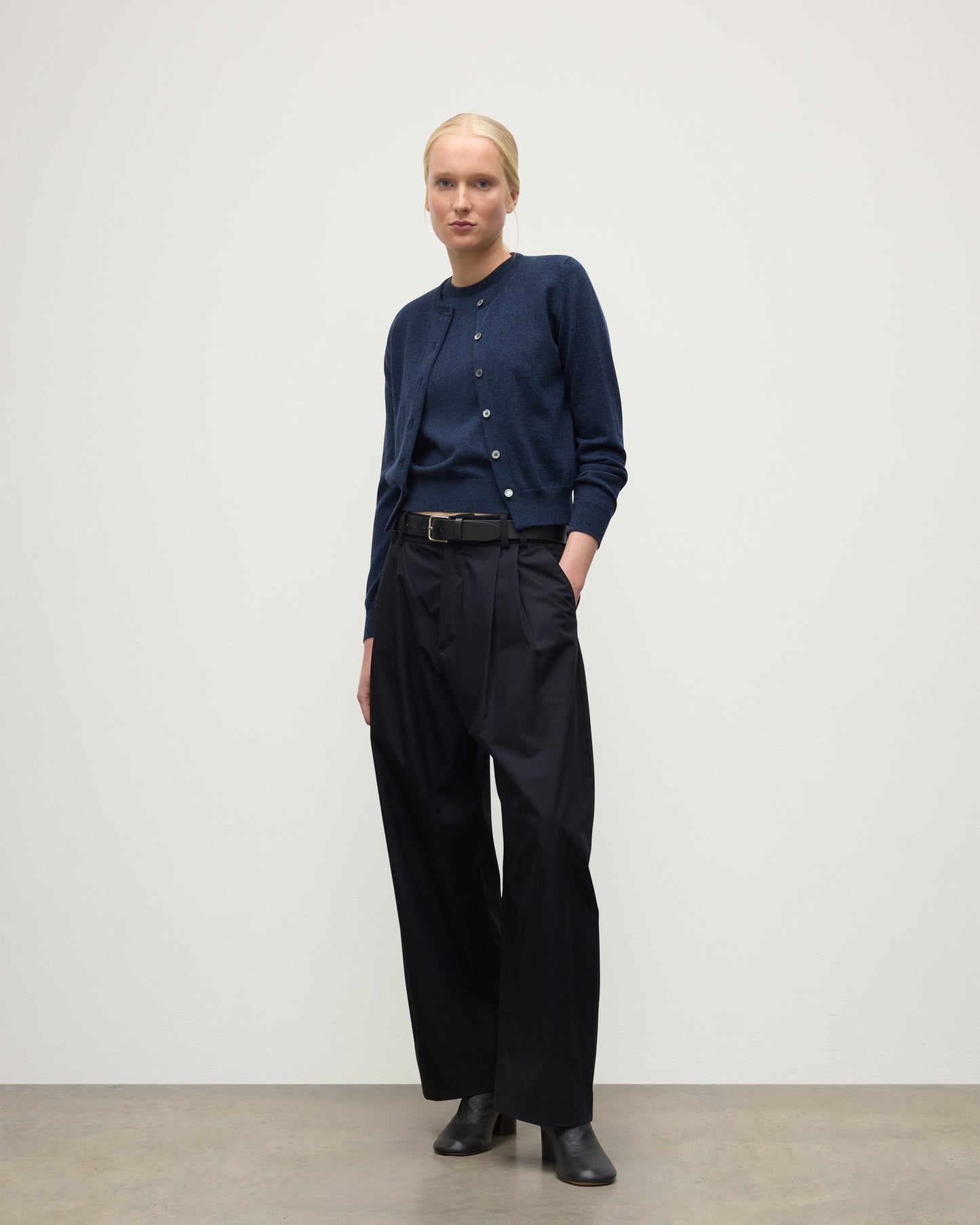 MODEL WEARING JOHNSTONS OF ELGIN WOMENS IRIS CLASSIC CREW CARDIGAN NAVY 100% CASHMERE, OVER A MATCHING SLEEVELESS TANK WITH NAVY TROUSERS, BLANK BOOTS KAP05704HD7350