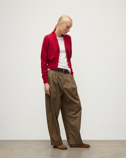 MODEL WEARS JOHNSTONS OF ELGIN WOMENS CRATHIE SHAWL CARDIGAN RED 100% CASHMERE WITH KILT PIN FASTENING, OVER A WHITE T-SHIRT AND BROWN WIDE LEG TROUSERS KAP05707SE5325