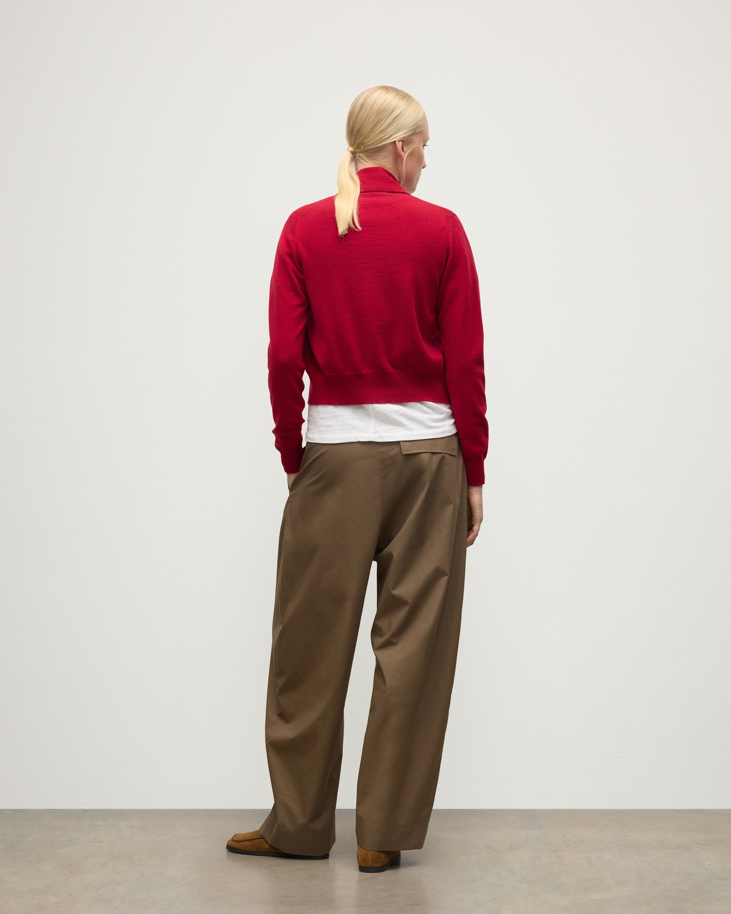 MODEL WEARS JOHNSTONS OF ELGIN WOMENS CRATHIE SHAWL CARDIGAN RED 100% CASHMERE WITH KILT PIN FASTENING, OVER A WHITE T-SHIRT AND BROWN WIDE LEG TROUSERS KAP05707SE5325