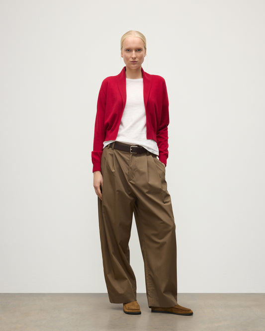 MODEL WEARS JOHNSTONS OF ELGIN WOMENS CRATHIE SHAWL CARDIGAN RED 100% CASHMERE WITH KILT PIN FASTENING, OVER A WHITE T-SHIRT AND BROWN WIDE LEG TROUSERS KAP05707SE5325