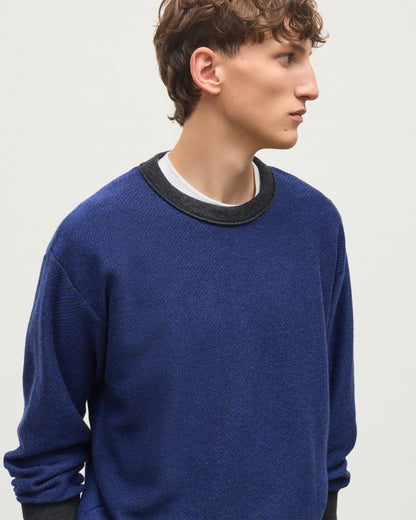 A man wearing a textured royal blue crewneck sweater with a contrasting black ribbed collar, layered over a white t-shirt, photographed against a light gray studio background. JOHNSTONS OF ELGIN LIDDELL SWEATSHIRT CASHMERE REVERSE TWILL STITCH SWEATSHIRT - 2 PLY GREY & BLUE 100% CASHMERE KAP05725Q26375