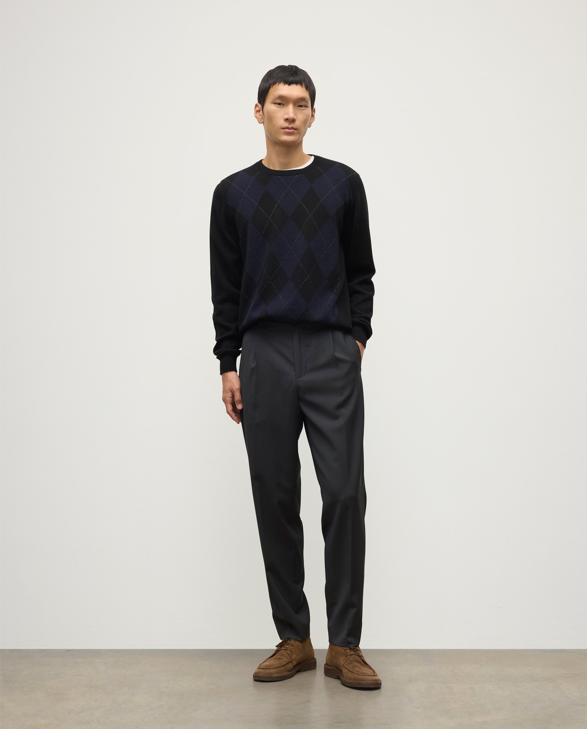 MODEL WEARING JOHNSTONS OF ELGIN MENS BLACK ARGYLL CREW SWEATER 100% CASHMERE OVER A WHITE T-SHIRT WITH NAVY TROUSERS KAP05747JU1599