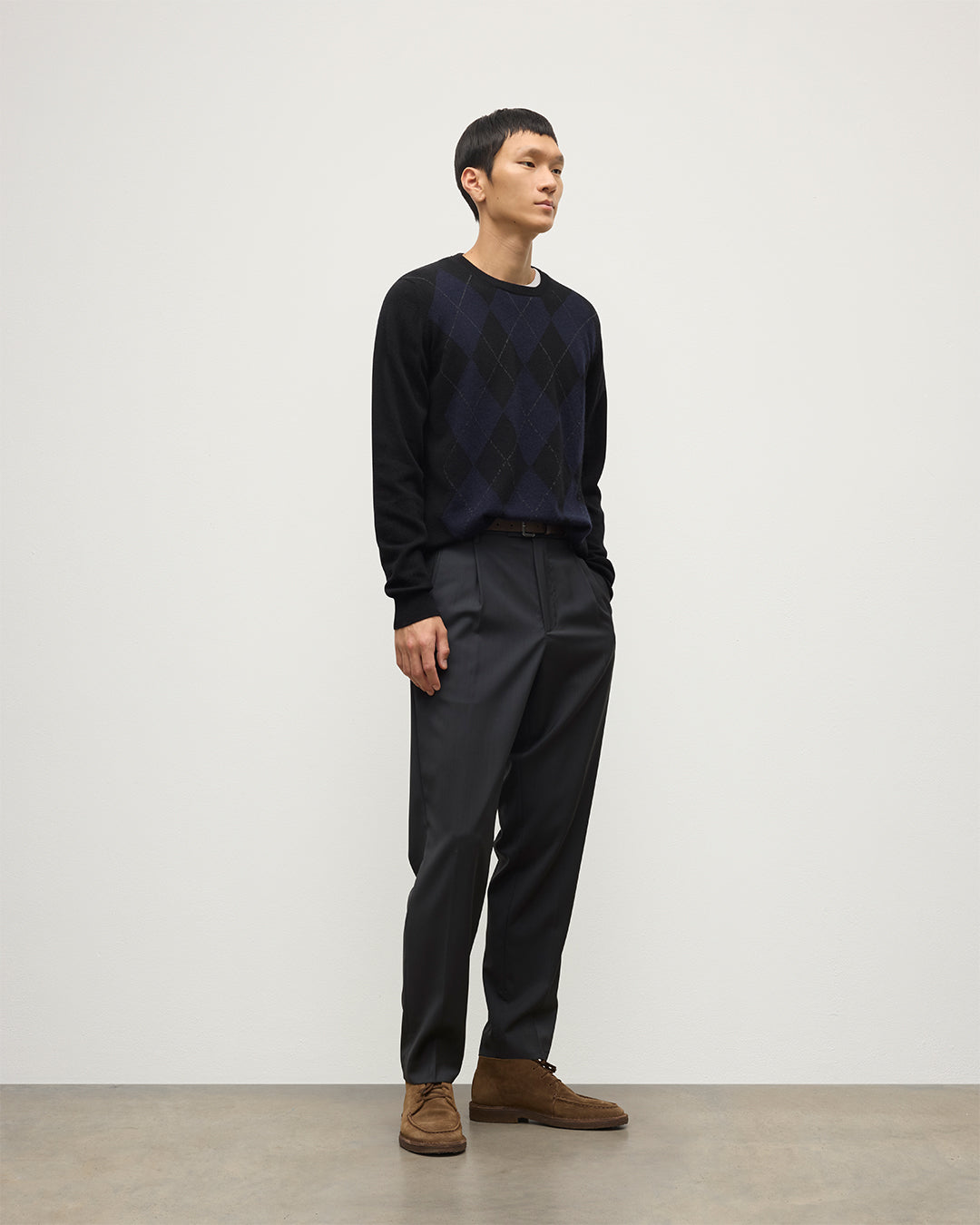 MODEL WEARING JOHNSTONS OF ELGIN MENS BLACK ARGYLL CREW SWEATER 100% CASHMERE OVER A WHITE T-SHIRT WITH NAVY TROUSERS KAP05747JU1599