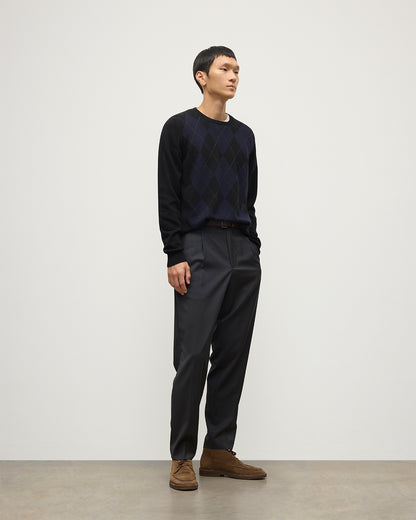 MODEL WEARING JOHNSTONS OF ELGIN MENS BLACK ARGYLL CREW SWEATER 100% CASHMERE OVER A WHITE T-SHIRT WITH NAVY TROUSERS KAP05747JU1599