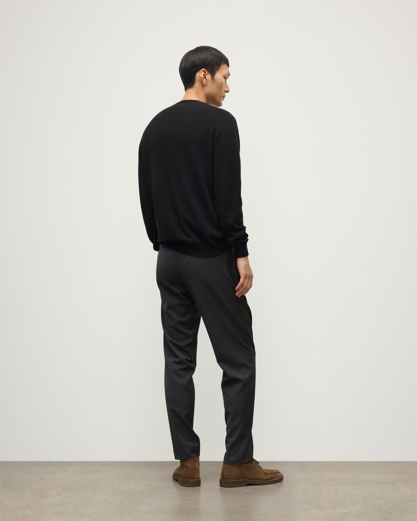 MODEL WEARING JOHNSTONS OF ELGIN MENS BLACK ARGYLL CREW SWEATER 100% CASHMERE OVER A WHITE T-SHIRT WITH NAVY TROUSERS KAP05747JU1599