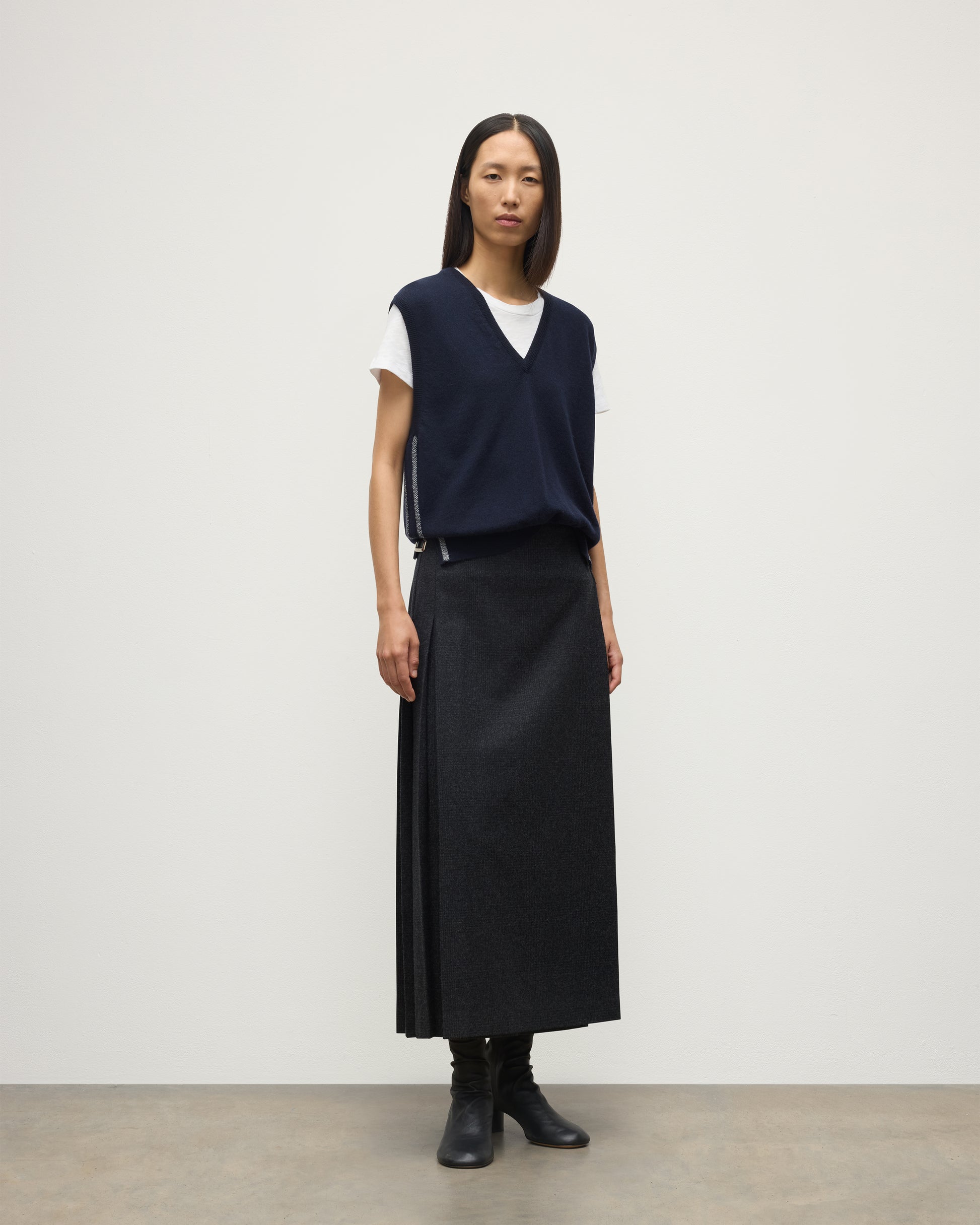 MODEL WEARS JOHYNSTONS OF ELGIN WOMENS TILDA SLEEVELESS VEE NAVY 100% CASHMERE WITH LE KILT JOHNSTONS OF ELGIN CASHMERE KILT IN CHARCOAL KAP05767Q25968