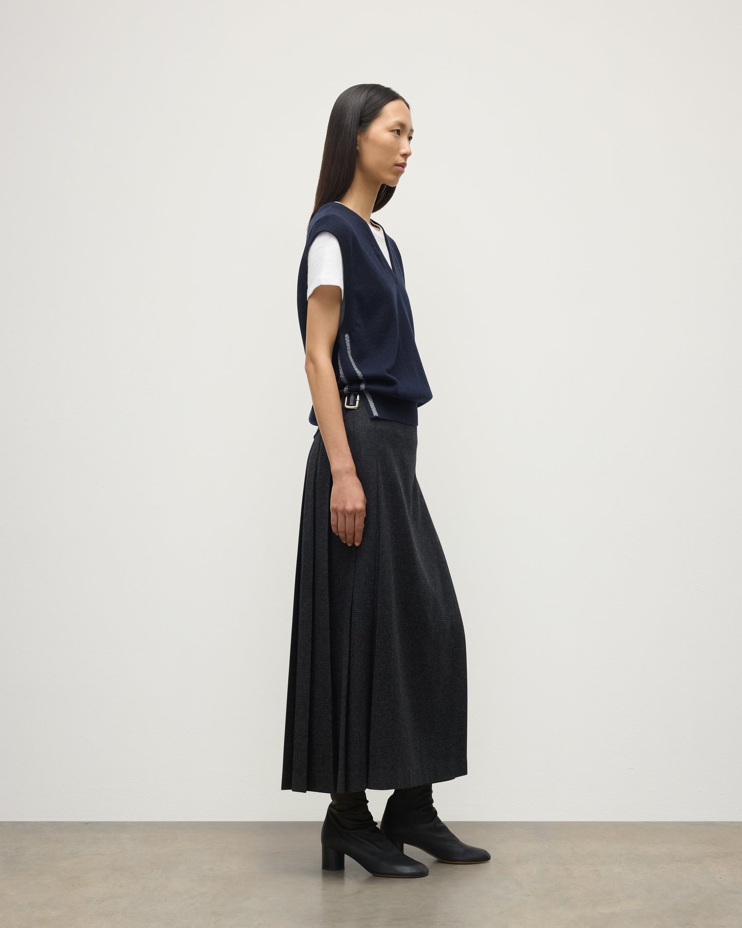 MODEL WEARS JOHYNSTONS OF ELGIN WOMENS TILDA SLEEVELESS VEE NAVY 100% CASHMERE WITH LE KILT JOHNSTONS OF ELGIN CASHMERE KILT IN CHARCOAL KAP05767Q25968