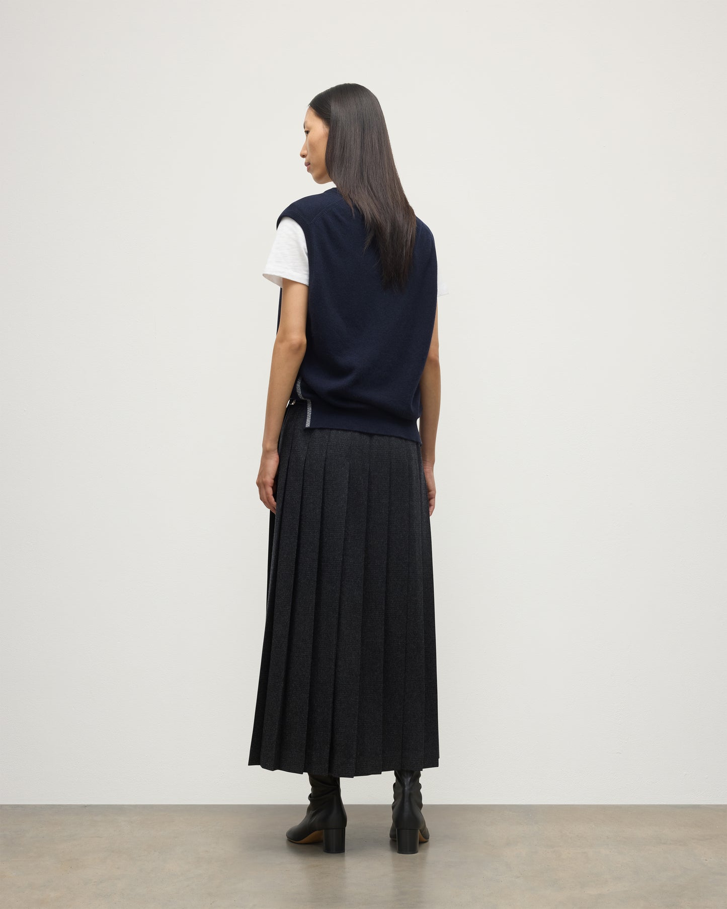 MODEL WEARS JOHYNSTONS OF ELGIN WOMENS TILDA SLEEVELESS VEE NAVY 100% CASHMERE WITH LE KILT JOHNSTONS OF ELGIN CASHMERE KILT IN CHARCOAL KAP05767Q25968