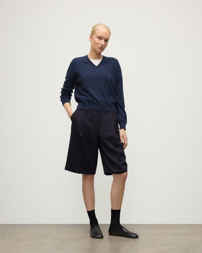 MODEL WEARING JOHNSTONS OF ELGIN WOMENS LUNAN CLASSIC VEE SWEATER NAVY 100% CASHMERE WITH LONG BLACK SHORTS KAP05807HD7350