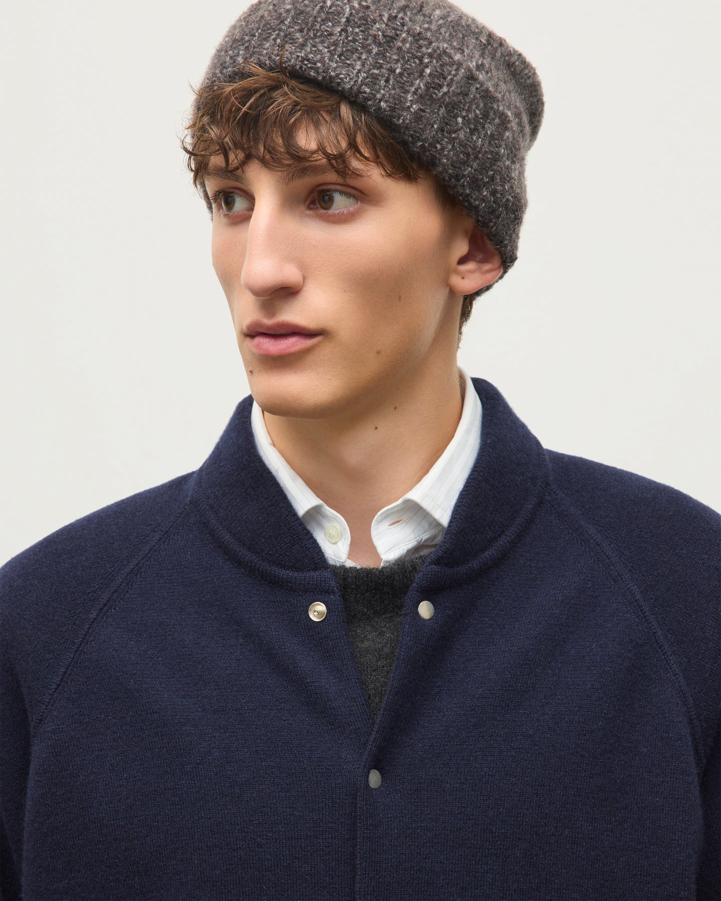 A man wearing a dark navy blue knit button-up cardigan over a white collared shirt and dark gray sweater, paired with a gray knit beanie, photographed against a light gray background. JOHNSTONS OF ELGIN KEPPIE BOMBER JACKET CASHMERE MILANO STITCH BOMBER JACKET - 2 PLY NAVY 100% CASHMERE KAP06008SD7666