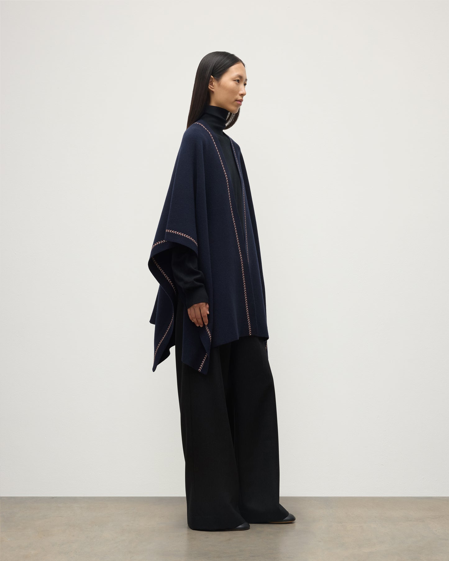 MODEL WEARS JOHNSTONS OF ELGIN WOMENS HAWK PONCHO NAVY 100% CASHMERE OVER NAVY ROLL NECK SWEATER AND NAVY TROUSERS KAU05769Q25973O/S