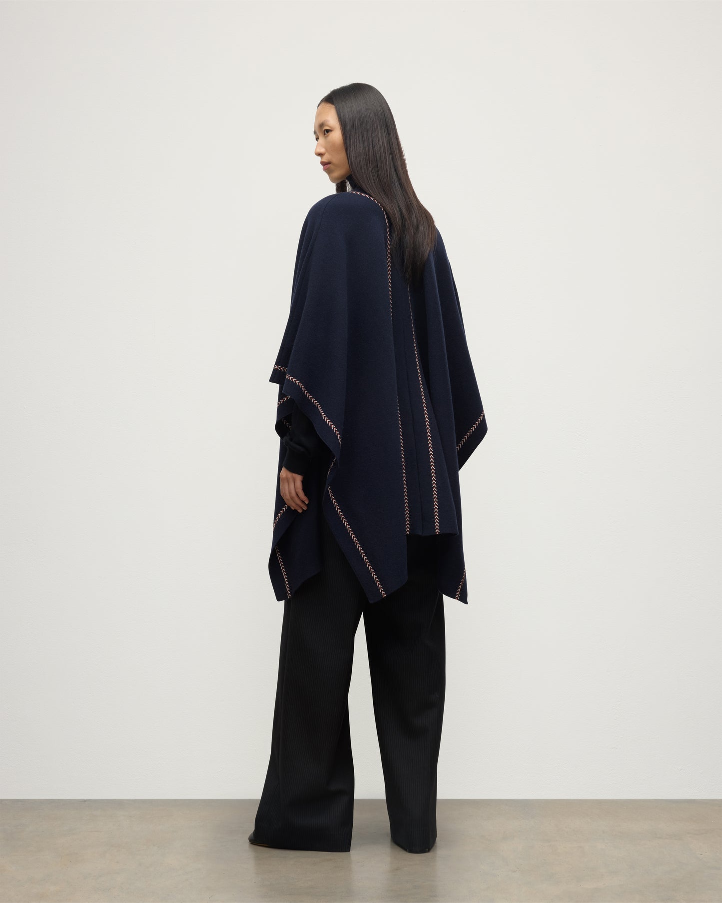 MODEL WEARS JOHNSTONS OF ELGIN WOMENS HAWK PONCHO NAVY 100% CASHMERE OVER NAVY ROLL NECK SWEATER AND NAVY TROUSERS KAU05769Q25973O/S