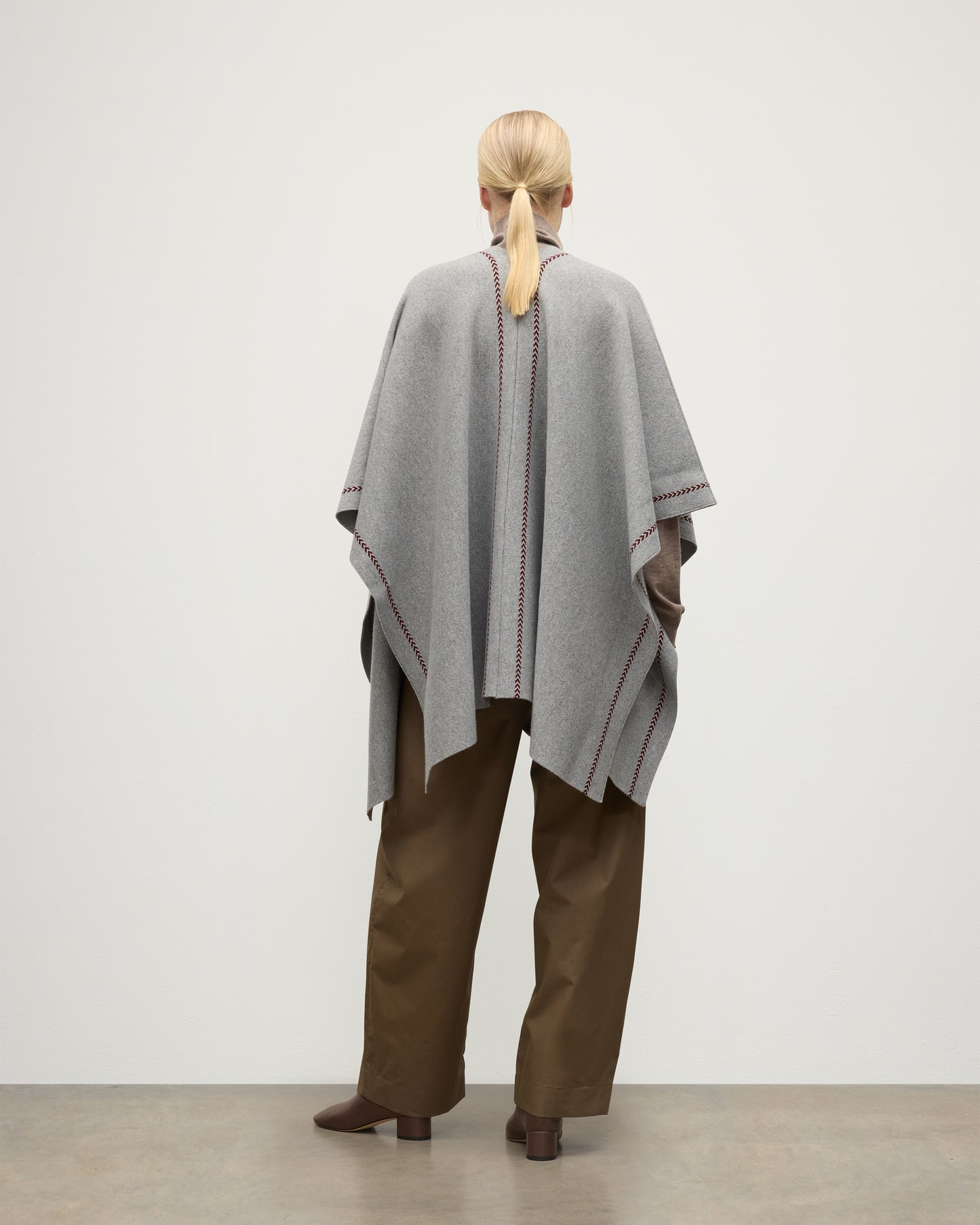 MODEL WEARS JOHNSTONS OF ELGIN WOMENS HAWK PONCHO LIGHT GREY 100% CASHMERE OVER A NATURAL CASHMERE SWEATER AND BROWN TROUSERS KAU05769Q25974O/S