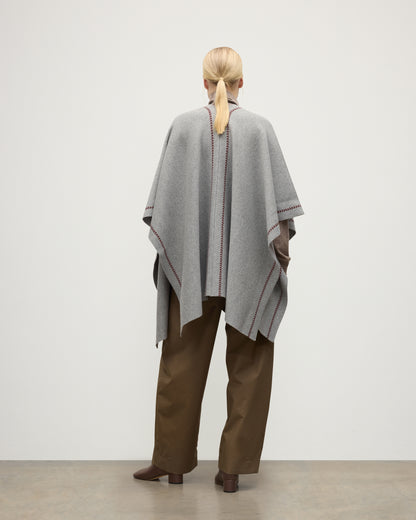MODEL WEARS JOHNSTONS OF ELGIN WOMENS HAWK PONCHO LIGHT GREY 100% CASHMERE OVER A NATURAL CASHMERE SWEATER AND BROWN TROUSERS KAU05769Q25974O/S
