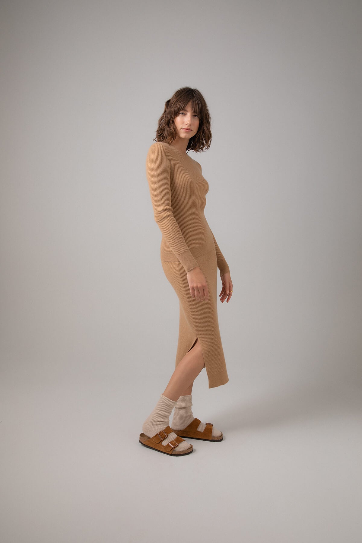 Side view of Johnstons of Elgin Ribbed Tube Cashmere Skirt in Camel worn with matching Slim Fit Cashmere Sweater on a grey background KBP00923HB4315