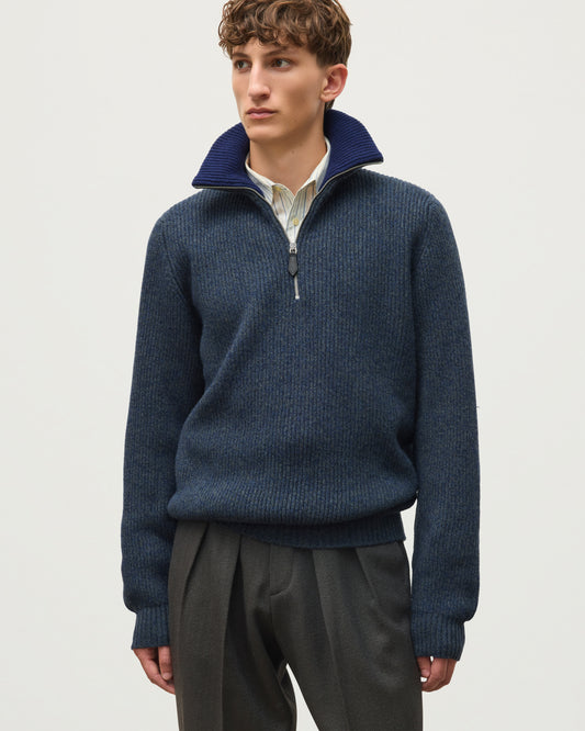 A man wearing a navy blue ribbed knit quarter-zip sweater with a stand-up collar, layered over a light-colored collared shirt and paired with dark gray trousers, photographed against a plain light gray studio background. JOHNSTONS OF ELGIN CHALMERS HALF ZIP SWEATER LAMBSWOOL RIBBED HALF ZIP SWEATER BLUE 100% LAMBSWOOL KDA00819Q26329