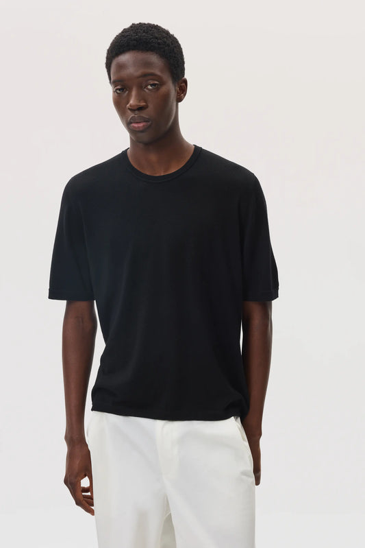 Model wearing Johnstons of Elgin SS25 Men's Knitwear Black Superfine Merino T-Shirt with white trousers  KDI00663SA7131