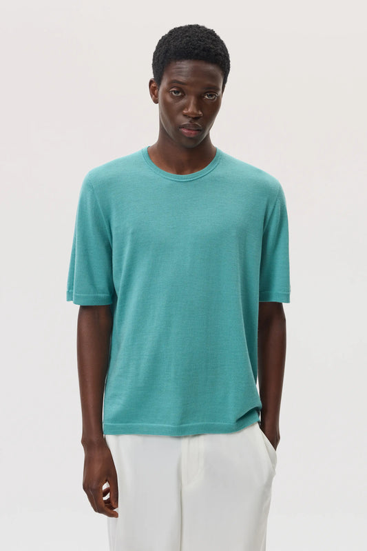 Model wearing Johnstons of Elgin SS25 Men's Knitwear Jade Superfine Merino T-Shirt with white trousers  KDI00663SC4641