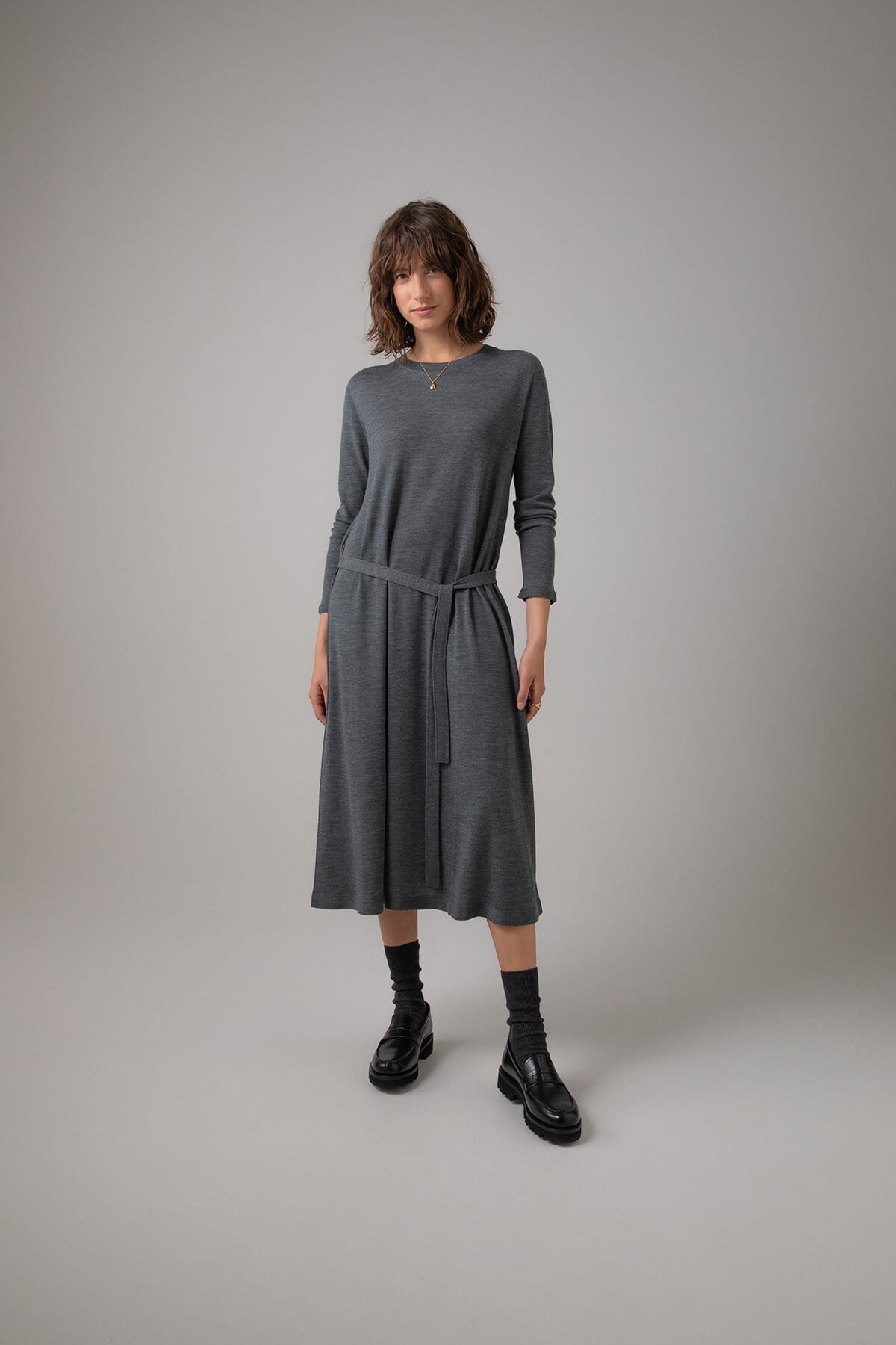 Johnstons of Elgin Women's Superfine Merino Belted T-Shirt Dress in Mid Grey worn with Black Socks & Shoes on a grey background KDI00685HA7166