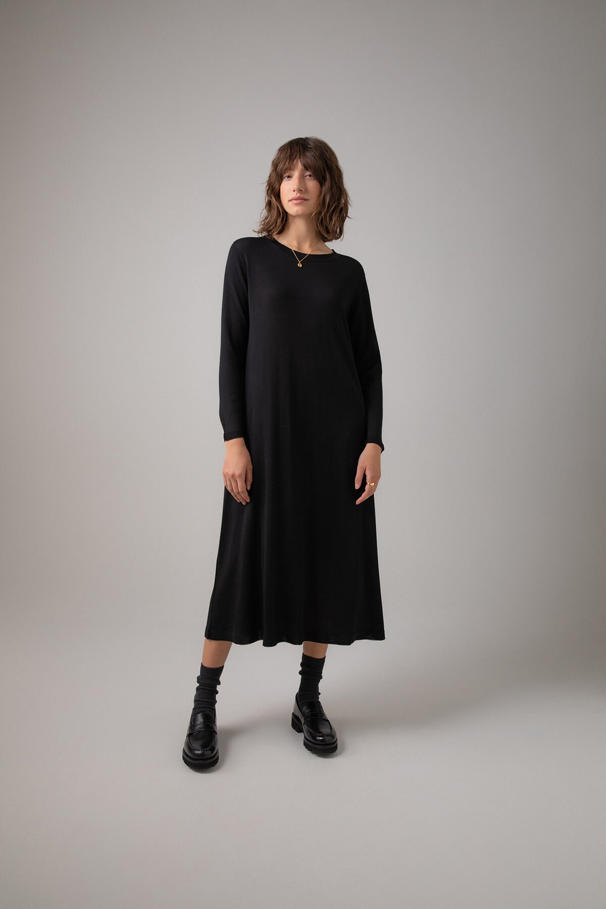 Johnstons of Elgin Women's Superfine Merino Belted T-Shirt Dress in Black worn unbelted with Black Socks & Shoes on a grey background KDI00685SA7131