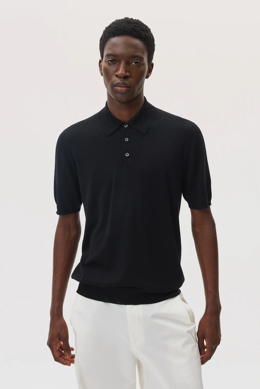 Model wears Johnstons of Elgin SS25 Men's Knitwear Black Superfine Merino Polo Shirt with white trousers  KDI00715SA7131