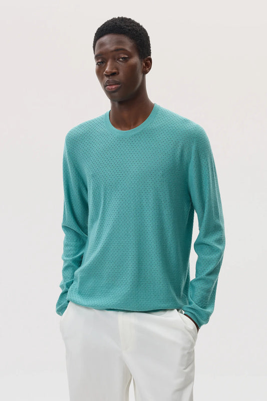 Model wearing Johnstons of Elgin SS25 Men's Knitwear Jade Superfine Merino Mesh Crew Neck Sweater with white trousers KDI00729SC4641