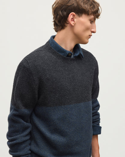 JOHNSTONS OF ELGIN OGILVIE CREW SWEATER LAMBSWOOL COLOURBLOCK CREW NECK SWEATER DARK GREY 100% LAMBSWOOL A man wearing a dark charcoal and navy blue color-block knit sweater over a matching navy collared shirt, paired with black trousers, against a plain light gray background. KDI00816Q26348 
