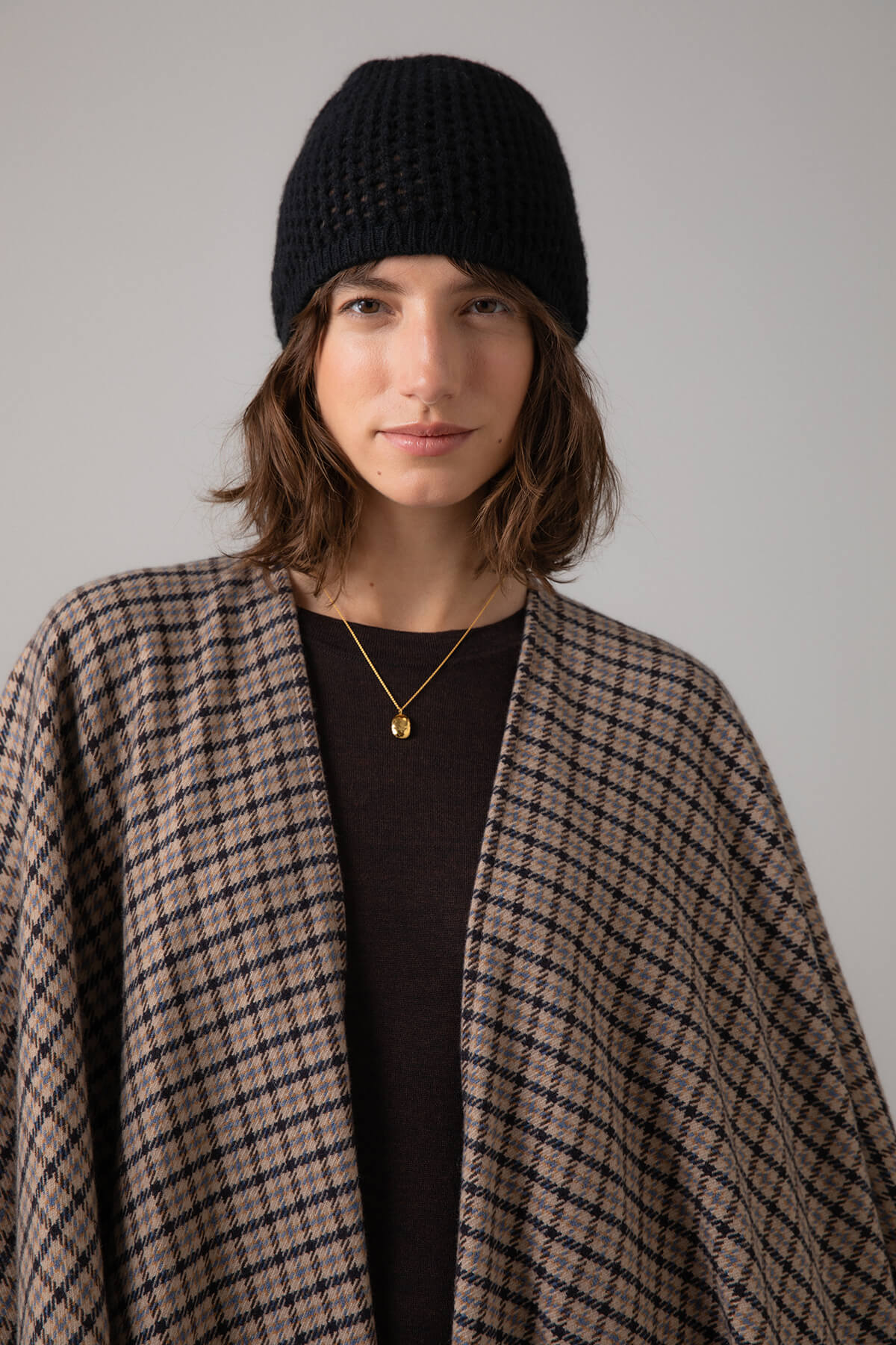 Johnstons of Elgin Cashmere Poncho Cape in Brown gunclub worn with a Black Crochet Cashmere Hat on a grey background TA000501RU7299ONE