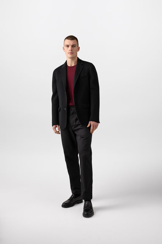 Johnstons of Elgin’s Men's Double Face Cashmere Jacket in Black on model wearing black trousers and red jumper on a white background TA000517RU6432