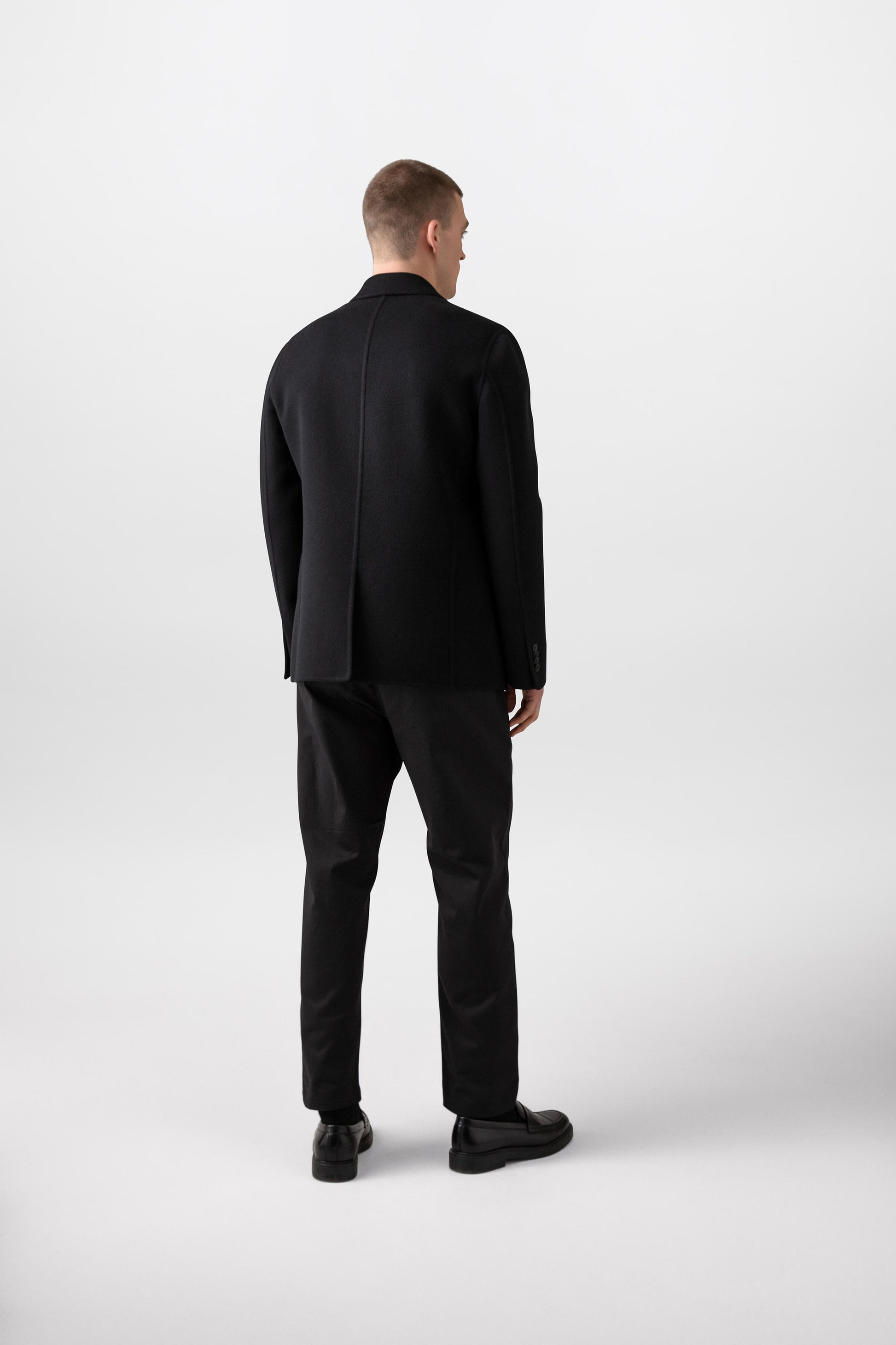 Johnstons of Elgin’s Men's Double Face Cashmere Jacket in Black on model wearing black trousers and red jumper on a white background TA000517RU6432