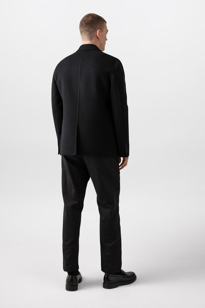 Johnstons of Elgin’s Men's Double Face Cashmere Jacket in Black on model wearing black trousers and red jumper on a white background TA000517RU6432