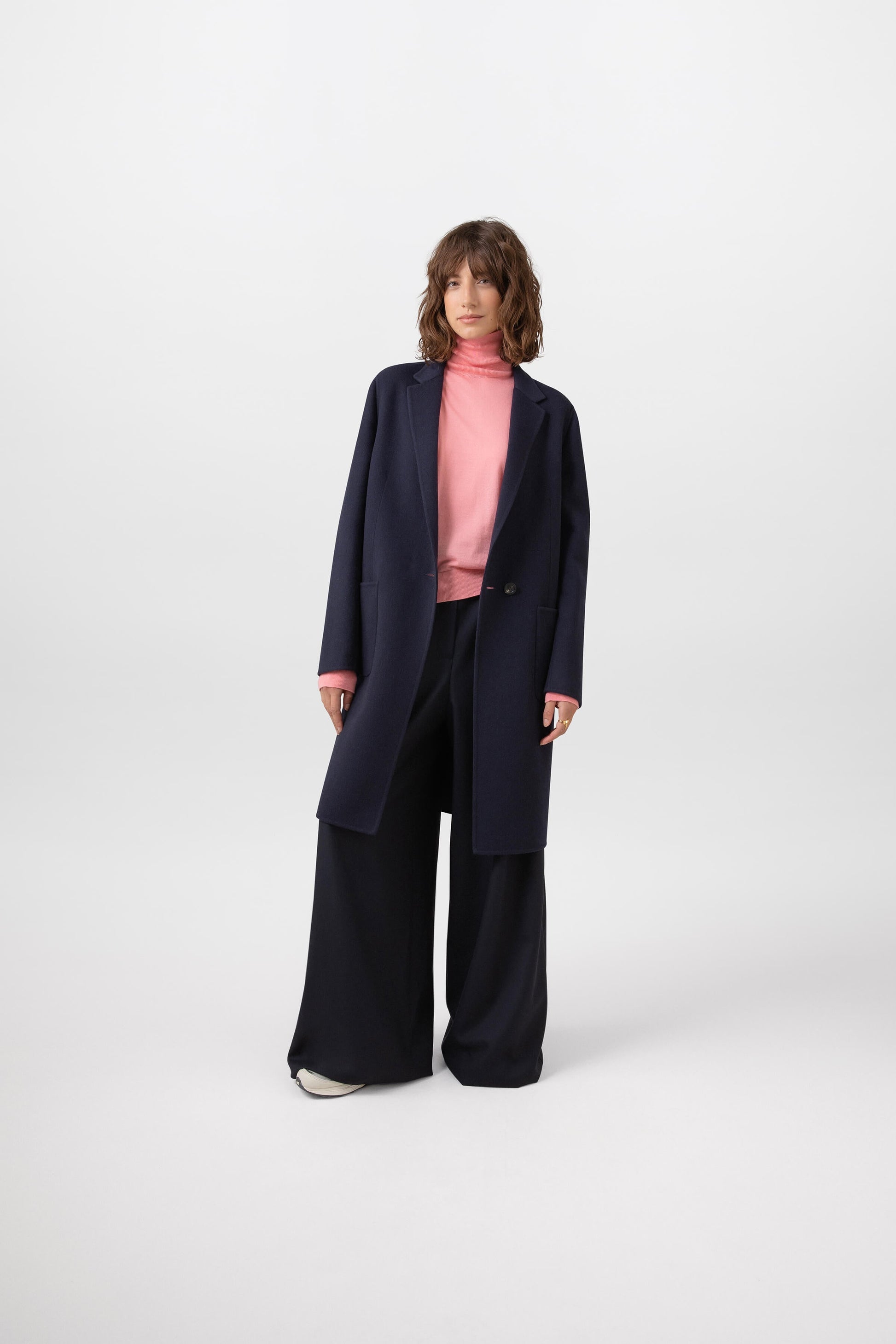 Johnstons of Elgin Women's Cashmere Crombie Coat in Navy worn with a Sea Pink Merino Roll Neck on a white background TA000520RU7291