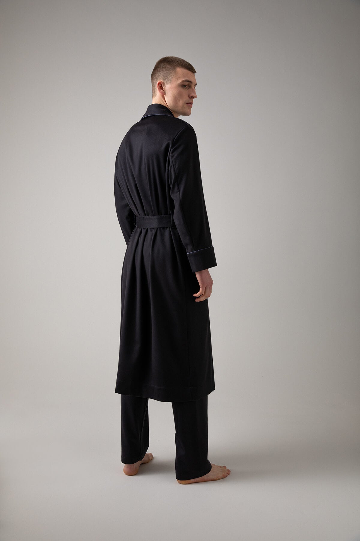 Johnstons of Elgin’s Men's Navy Cashmere Dressing Gown with Silk Lining on model wearing navy bottoms on a grey background TA000472RU65880